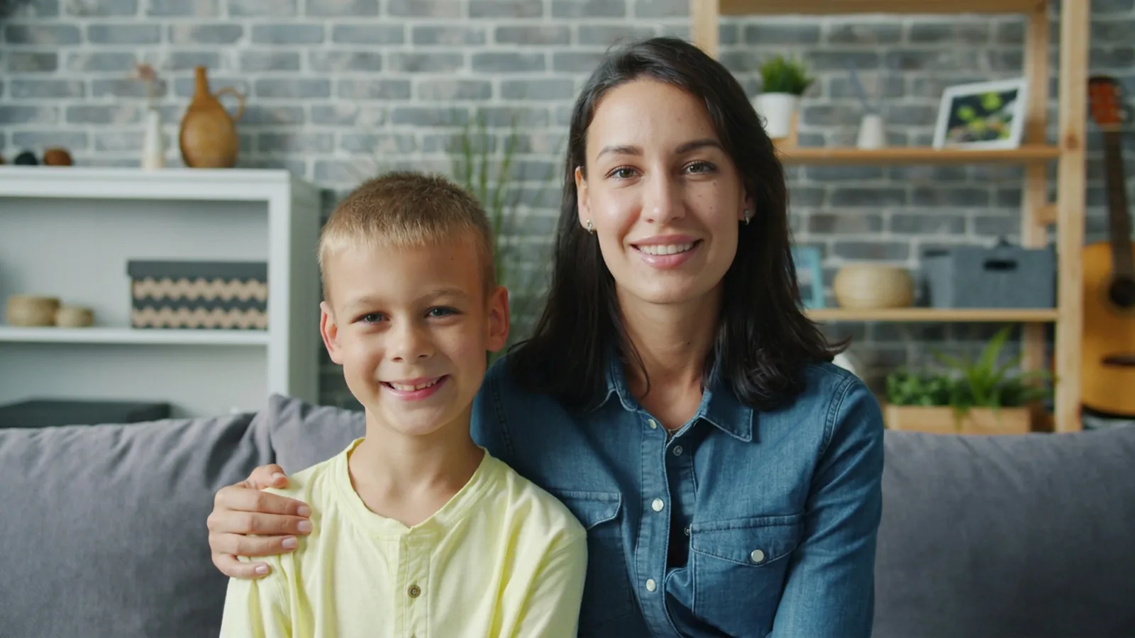 A smiling mother with her arm around her young son on a living room couch